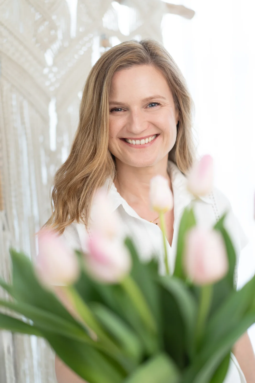 Joanna śmieje się, trzymając bukiet różowych tulipanów blisko twarzy.
